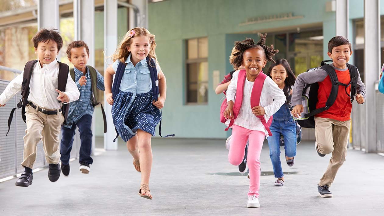 6 kids running in the school hallway wearing schoolbags